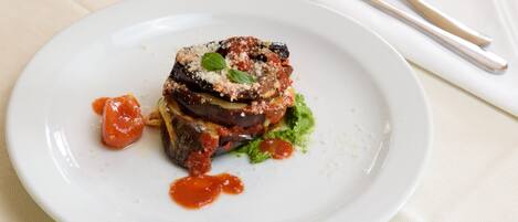 Un plato con berenjena rellena, adornado con hierbas y salsa, sobre un plato blanco.