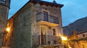 Un edificio de piedra con un balcón, un ventanal pequeño y una puerta.