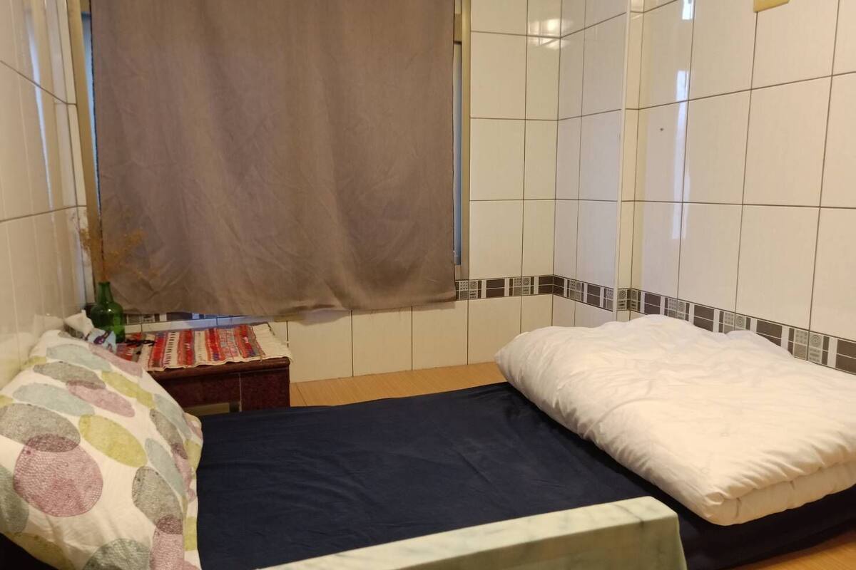 A small, clean room with two beds, a nightstand, and a window with a curtain.