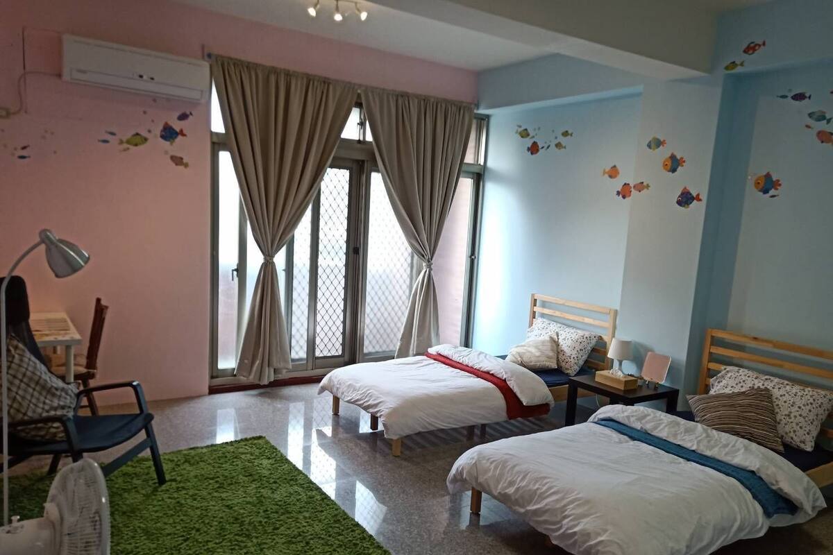 A bedroom with two beds, a desk, a chair, and a window with curtains.