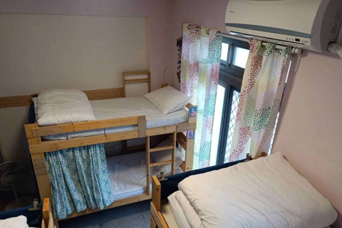 A dormitory room with bunk beds, a window with patterned curtains, and an air conditioning unit.