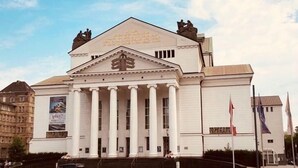Ein großes, weißes Gebäude mit Säulen und einem dreieckigen Giebel, gekrönt von einer Statue.