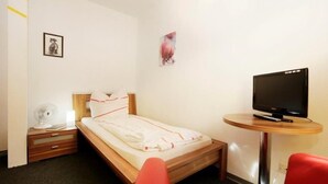 Ein Hotelzimmer mit einem Bett, einem Nachttisch mit Ventilator, einem Fernseher auf einem kleinen Tisch und einem roten Sessel.