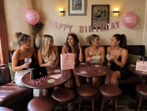 A group of women seated at round tables in a restaurant with a 'Happy Birthday' banner and balloons. - The Kings Cross Hotel (Blackpool)
