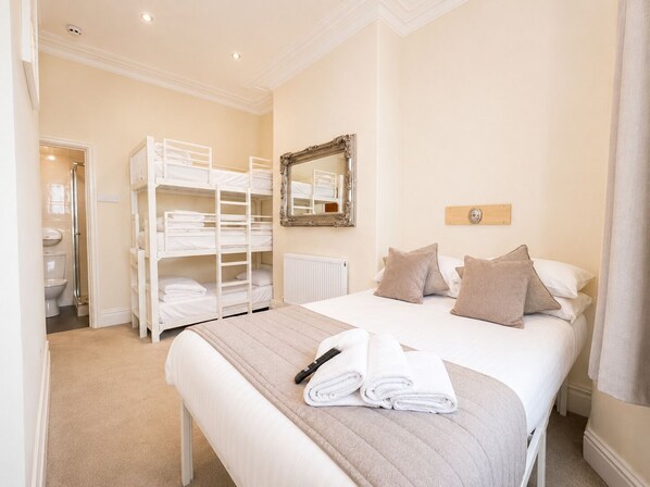 A hotel room with bunk beds, a large bed, a mirror, and a radiator.