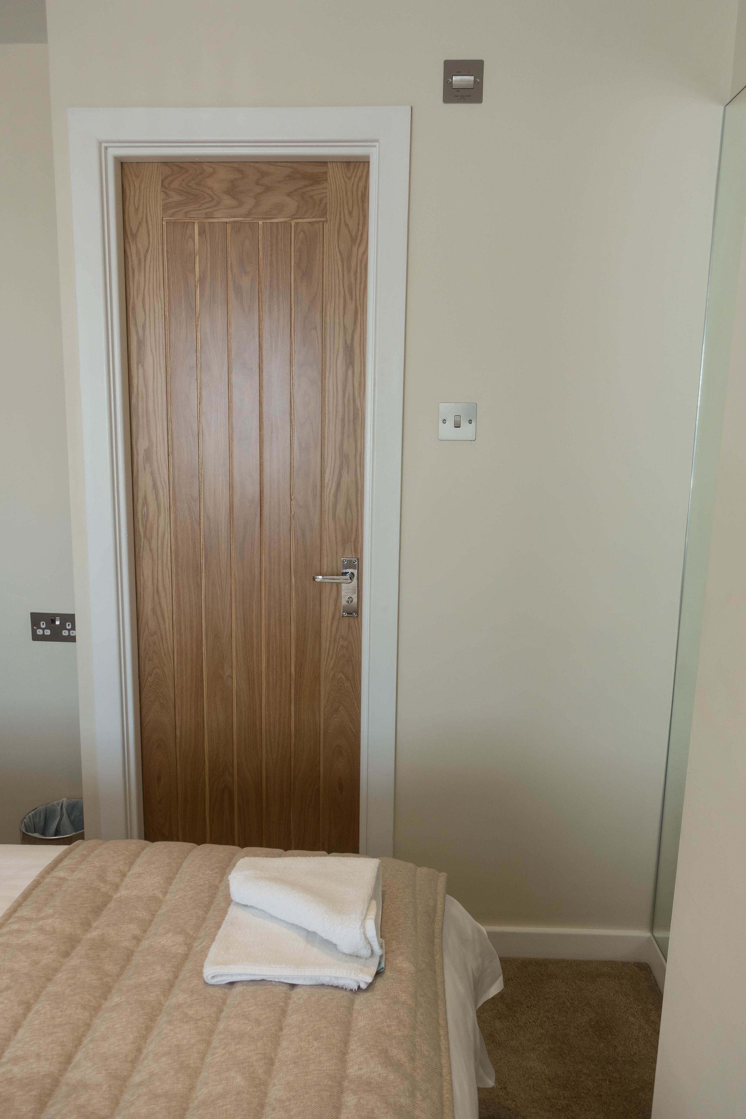 Un dormitorio con una puerta de madera, una cama con colcha color crema y una toalla blanca sobre la cama.