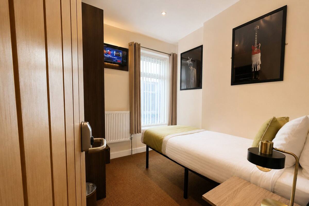 A hotel room with a bed, a bedside table with a lamp, a TV, and a window with curtains.