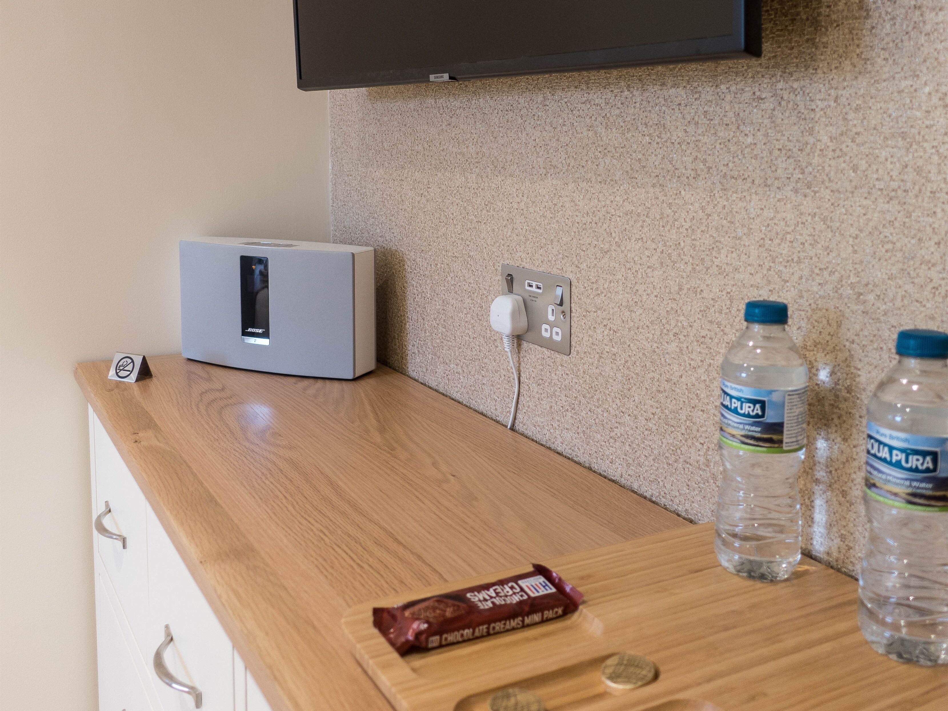 Una barra de madera con un altavoz, un enchufe, dos botellas de agua y una barra de chocolate.