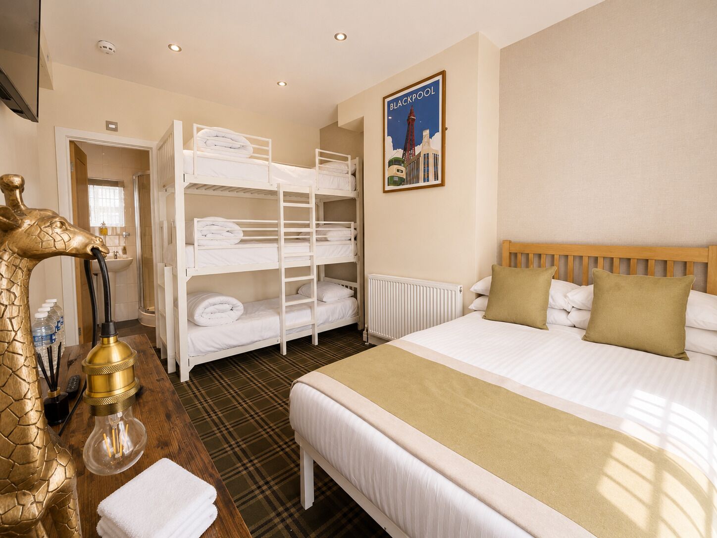 Une chambre d’hôtel avec un lit superposé, un lit simple, un radiateur, une affiche de Blackpool et une lampe décorative.