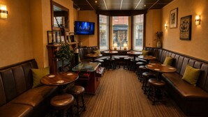 Um espaço de bar acolhedor, com assentos em couro, mesas redondas e uma tela de televisão.