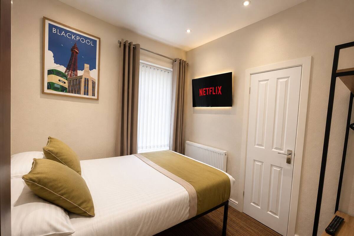 A hotel room with a bed, a poster of Blackpool, a Netflix sign, and a door.