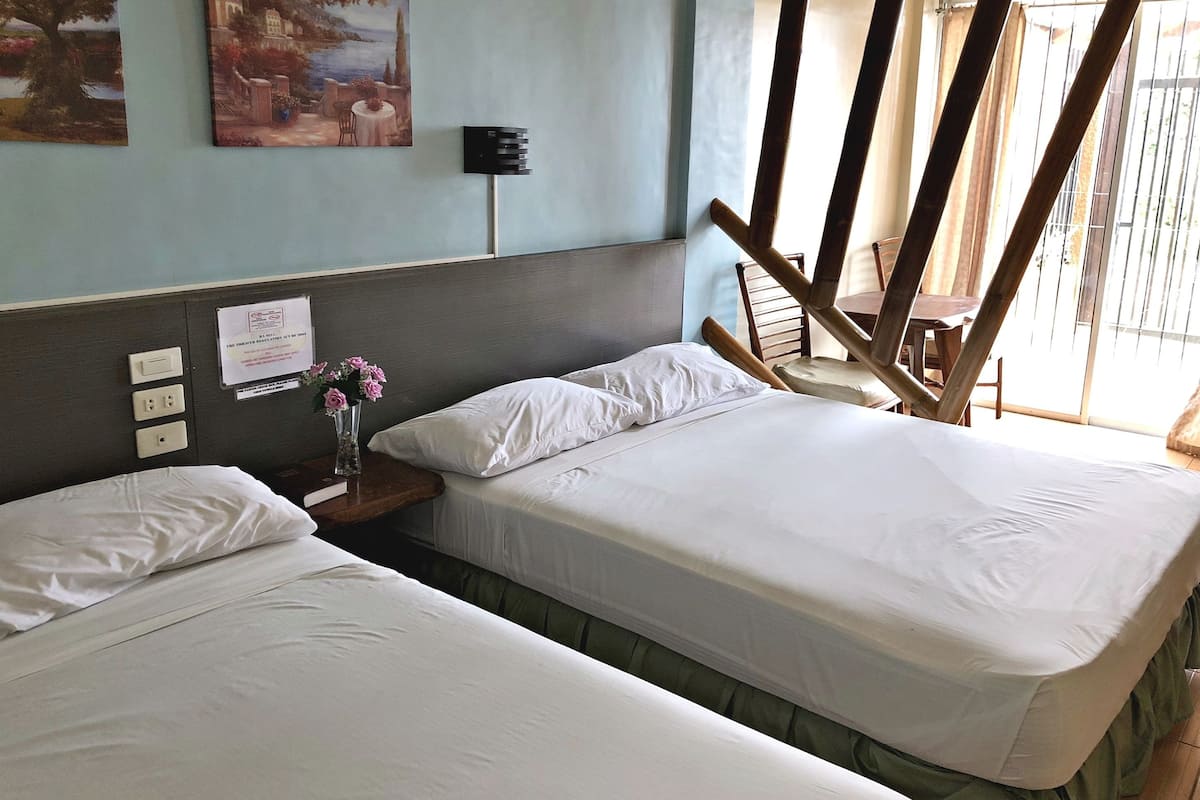 A hotel room with two beds, a nightstand with a vase of flowers, a painting on the wall, and a window with a view.