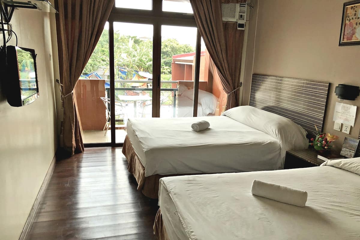 A hotel room with two beds, a wooden floor, a view of the outside, and a window with curtains.