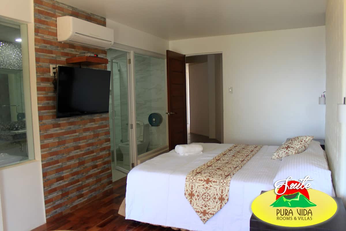 A hotel room with a bed, a TV mounted on the wall, and a glass shower enclosure.