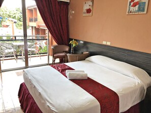 A hotel room with a large bed, a chair, a small table with a vase, and a balcony with chairs and a table. - Pura Vida Resort (Tagaytay)
