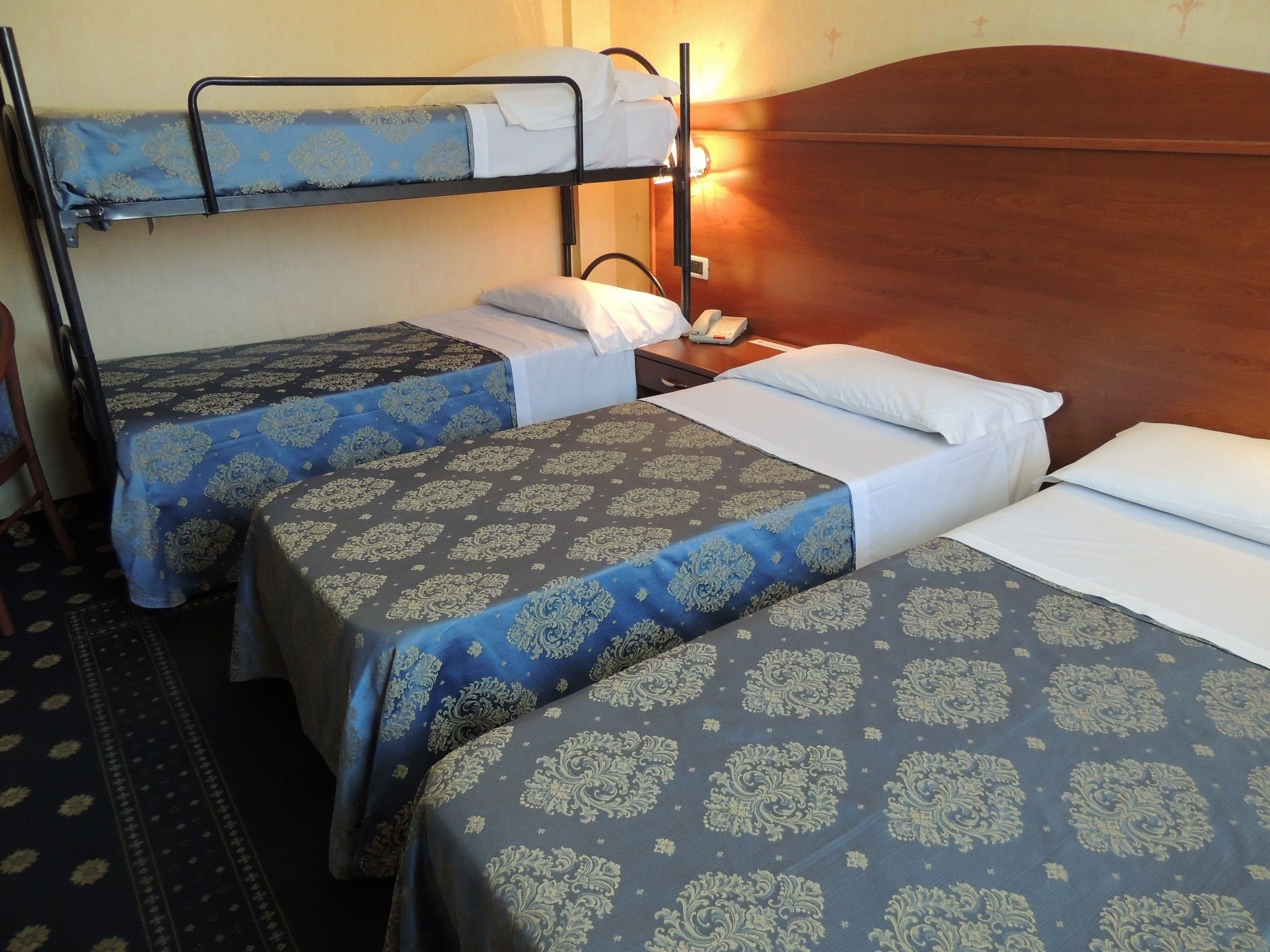 A room with two bunk beds, each with a patterned bedspread, a bedside table with a lamp, and a telephone.