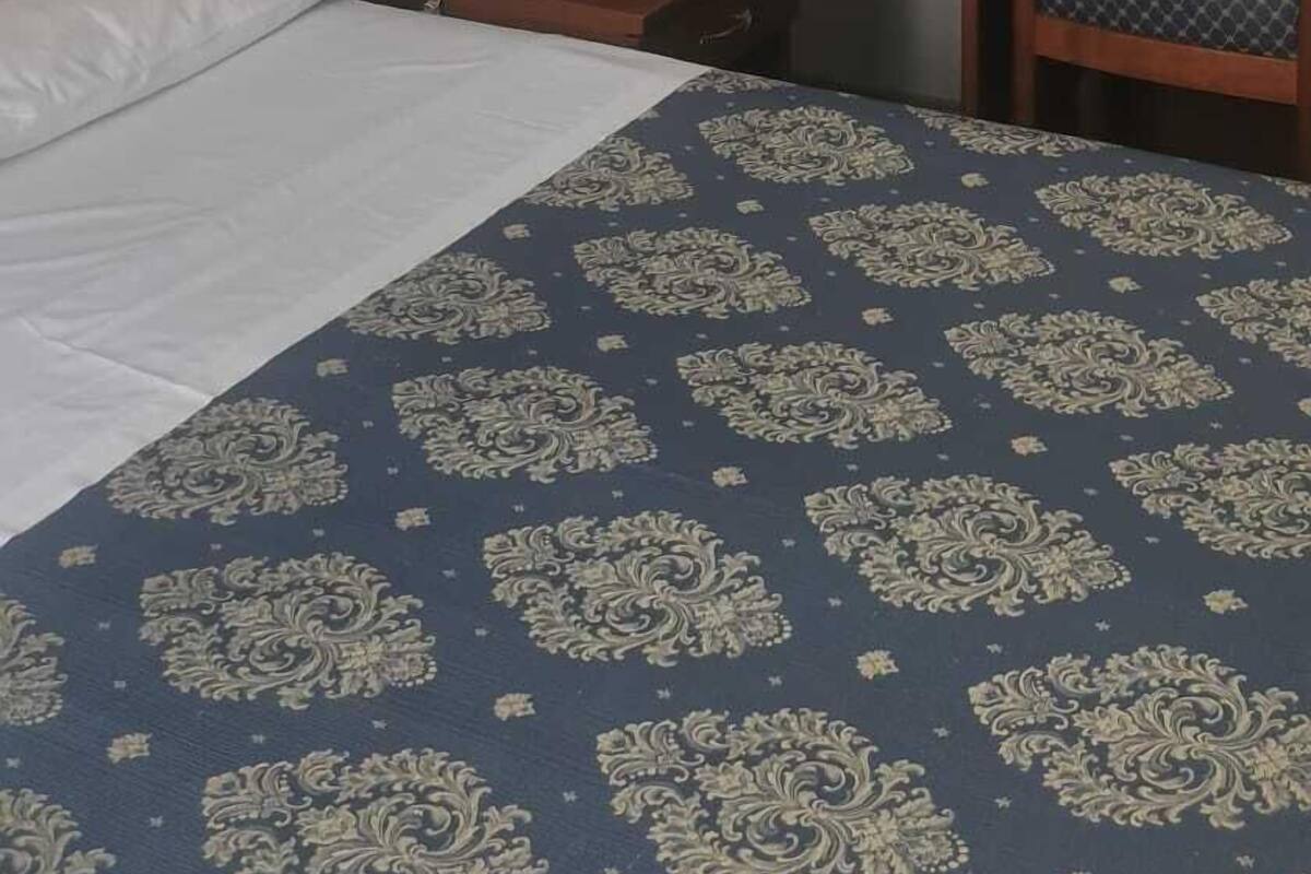 A hotel room with a bed, a desk with a chair, a small table, a telephone, and a mirror.