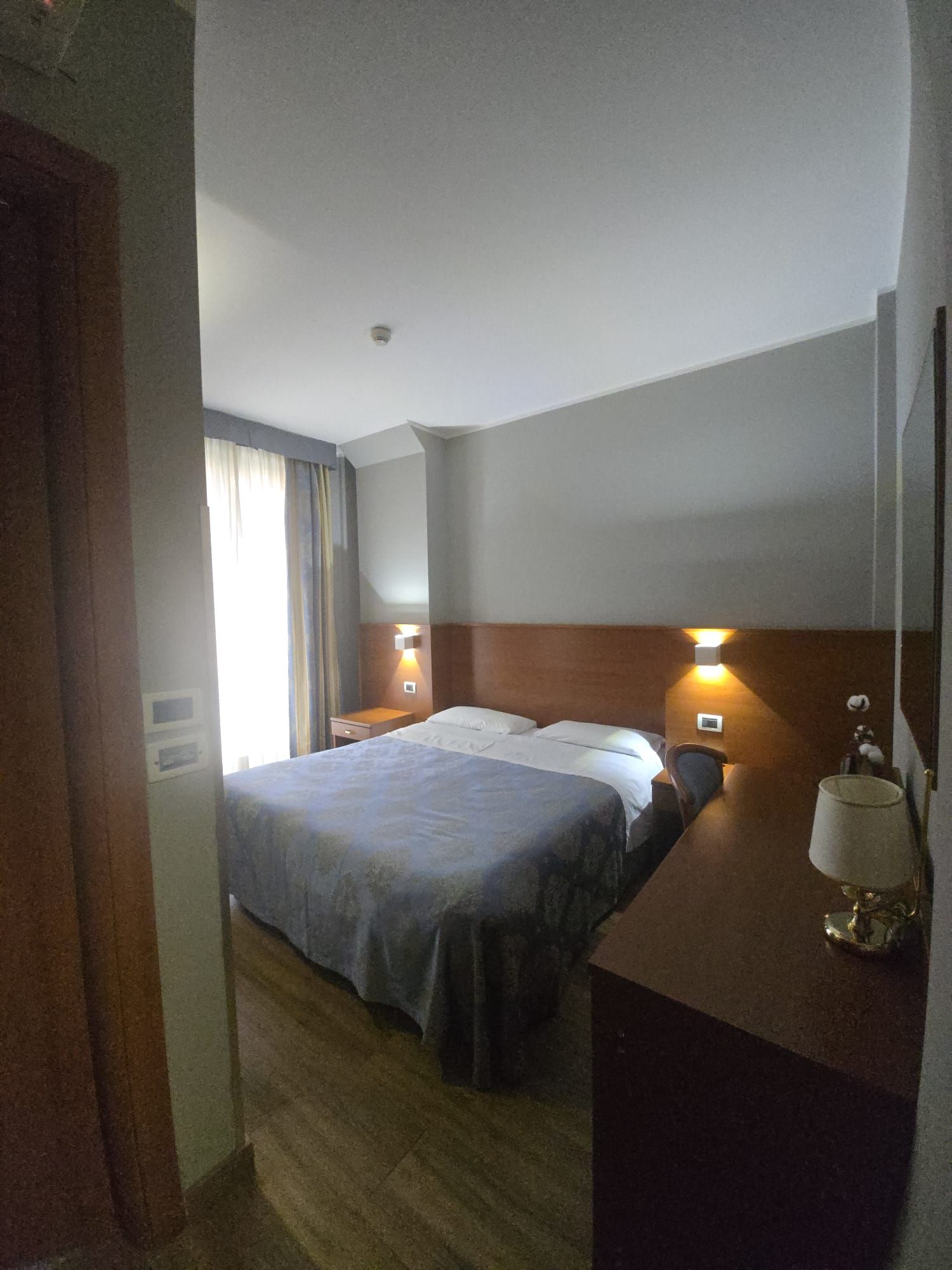 Habitación de hotel con una cama, mesitas de noche, un escritorio con lámpara y un espejo.