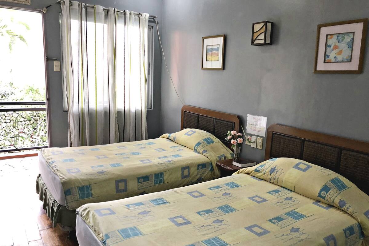 Une chambre avec deux lits, une fenêtre avec des rideaux et un mur orné de tableaux.