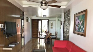A spacious living area with a red sofa, a glass coffee table, a ceiling fan, and a dining area with wooden furniture. - Pura Vida Villas (Tagaytay)