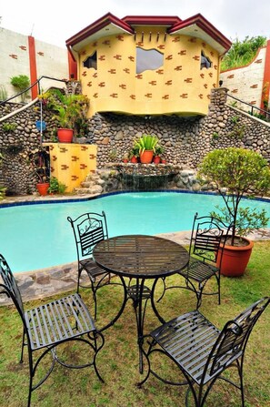 Área da piscina com parede de pedra, pequena cascata e mobiliário de exterior.