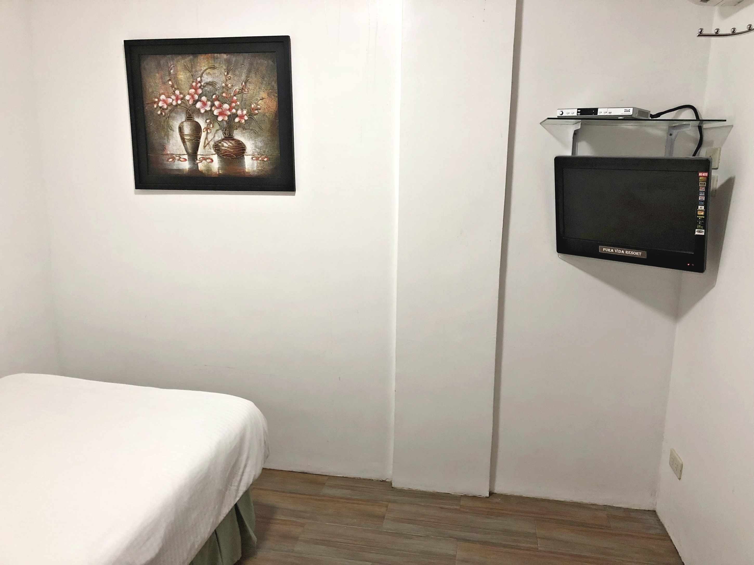 Una habitación pequeña y limpia con una cama, un televisor de pared y una obra de arte enmarcada.