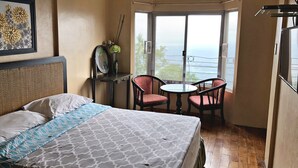 A hotel room with a bed, a small table with two chairs, a window with a view of the sea, and a framed picture on the wall. - Pura Vida Villas (Tagaytay)