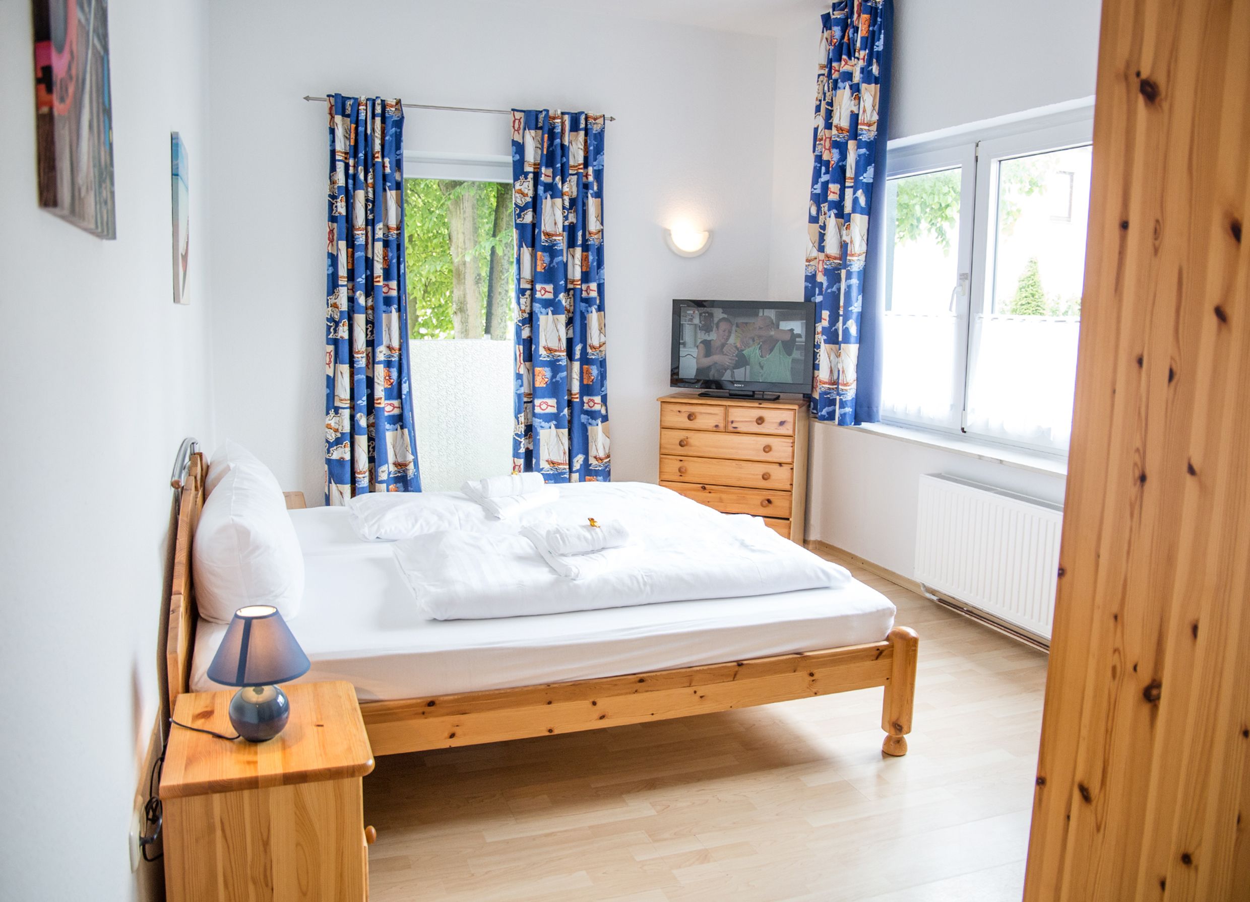 A bedroom with a wooden bed, a wooden dresser, a TV, and curtains.