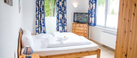 A bedroom with a wooden bed, a wooden dresser, a TV, and curtains.