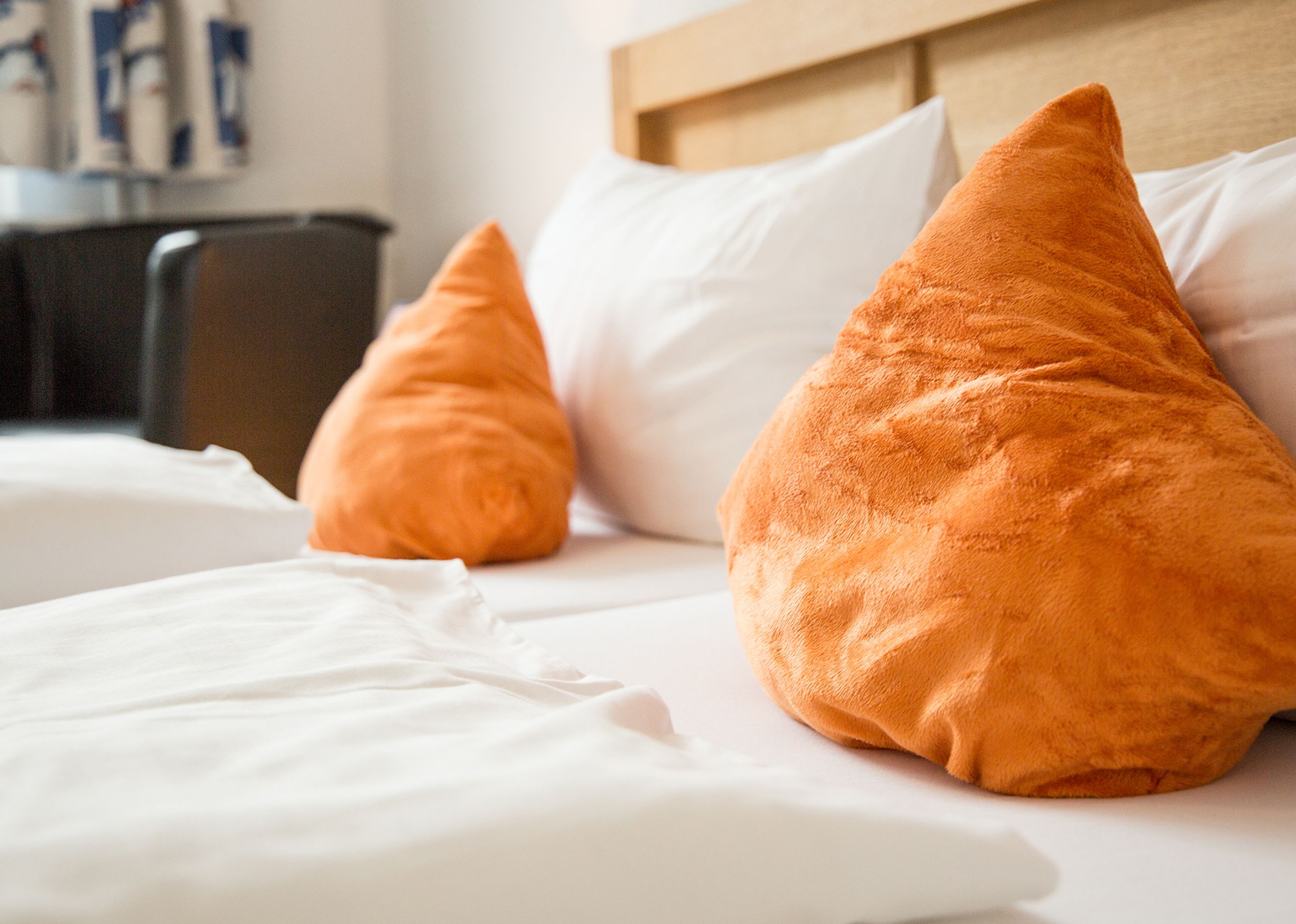 Una habitación de hotel con una cama, ropa de cama blanca y dos almohadas naranjas.