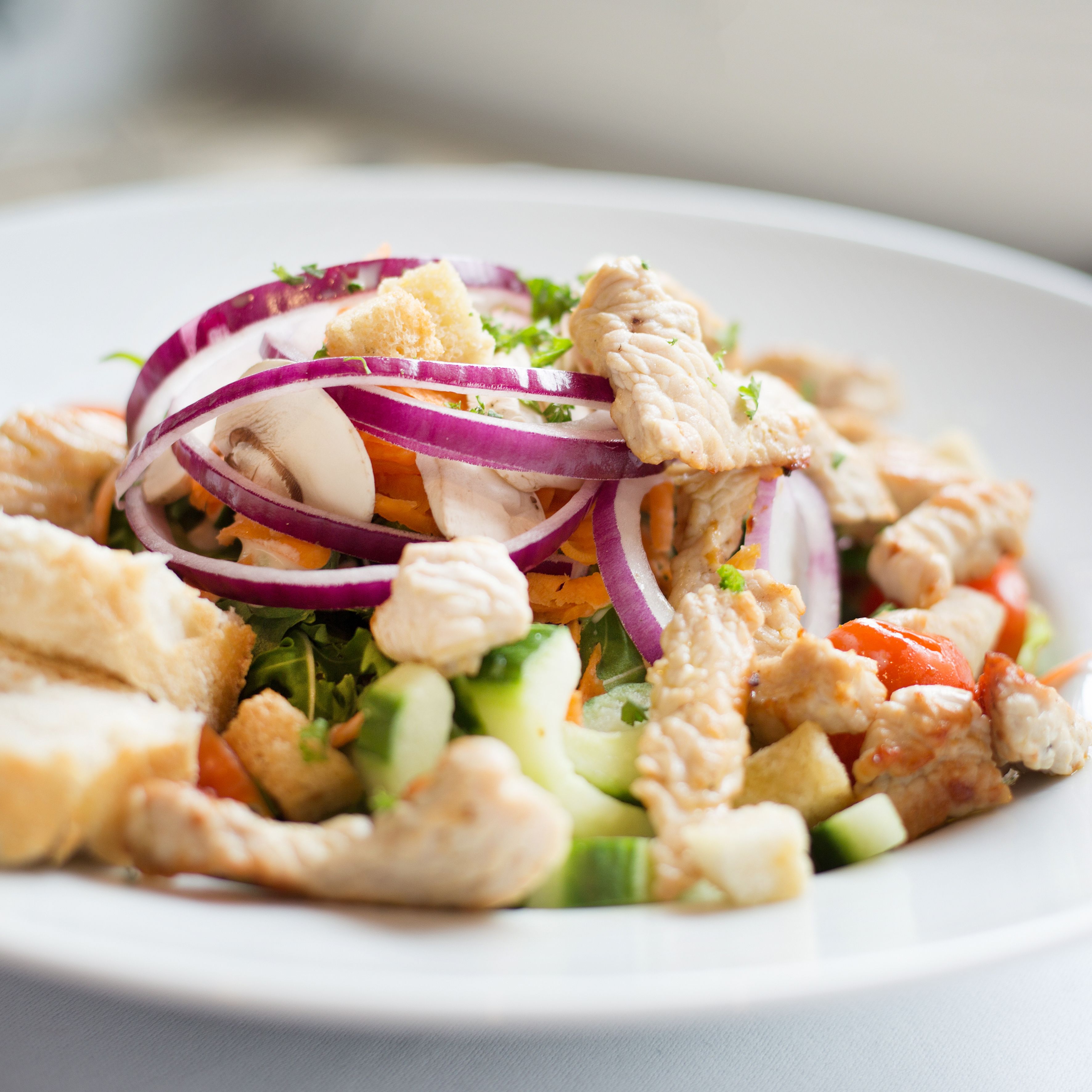 A plate of chicken salad with vegetables and croutons.