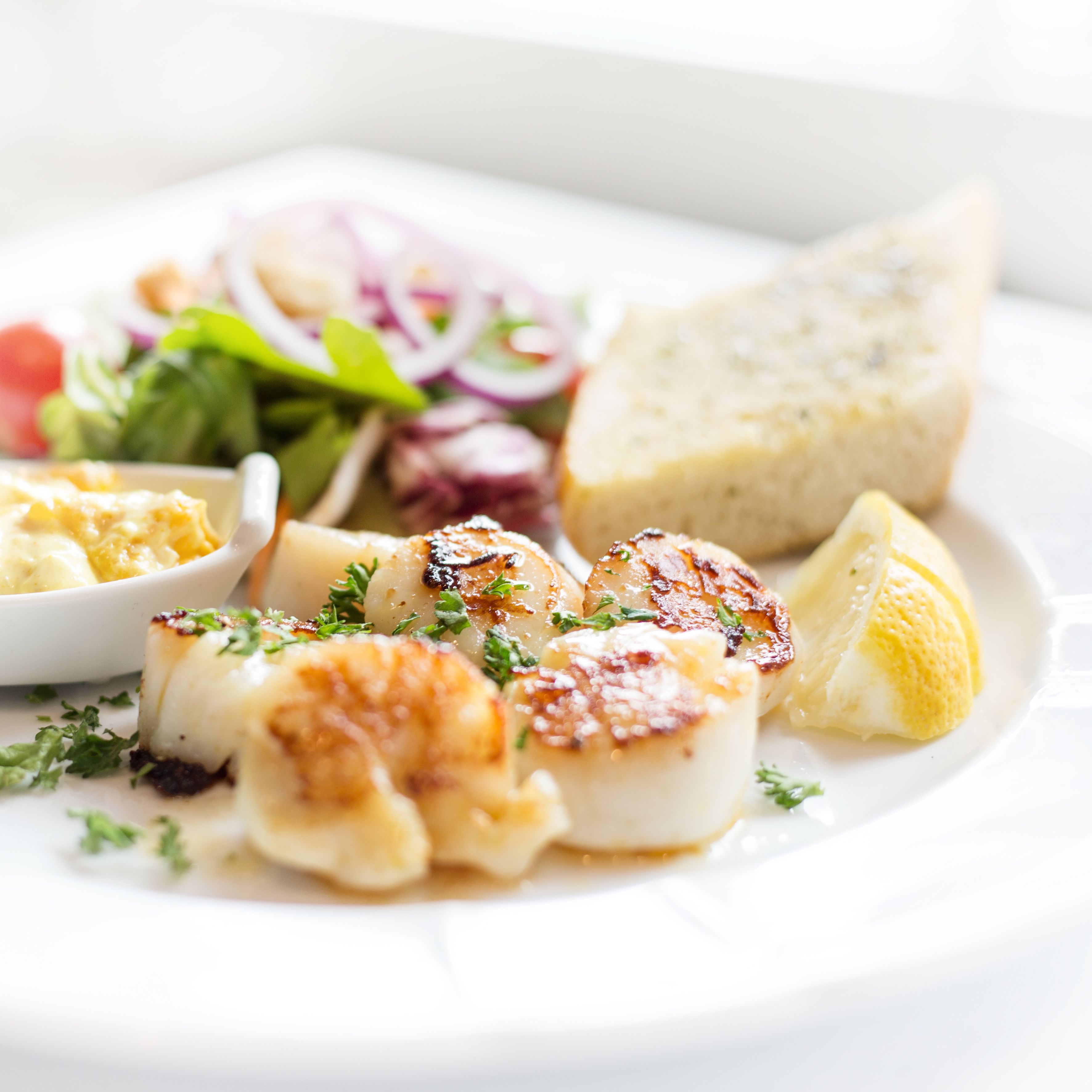 Ein Teller mit gegrilltem Fisch, Salat und Brot.