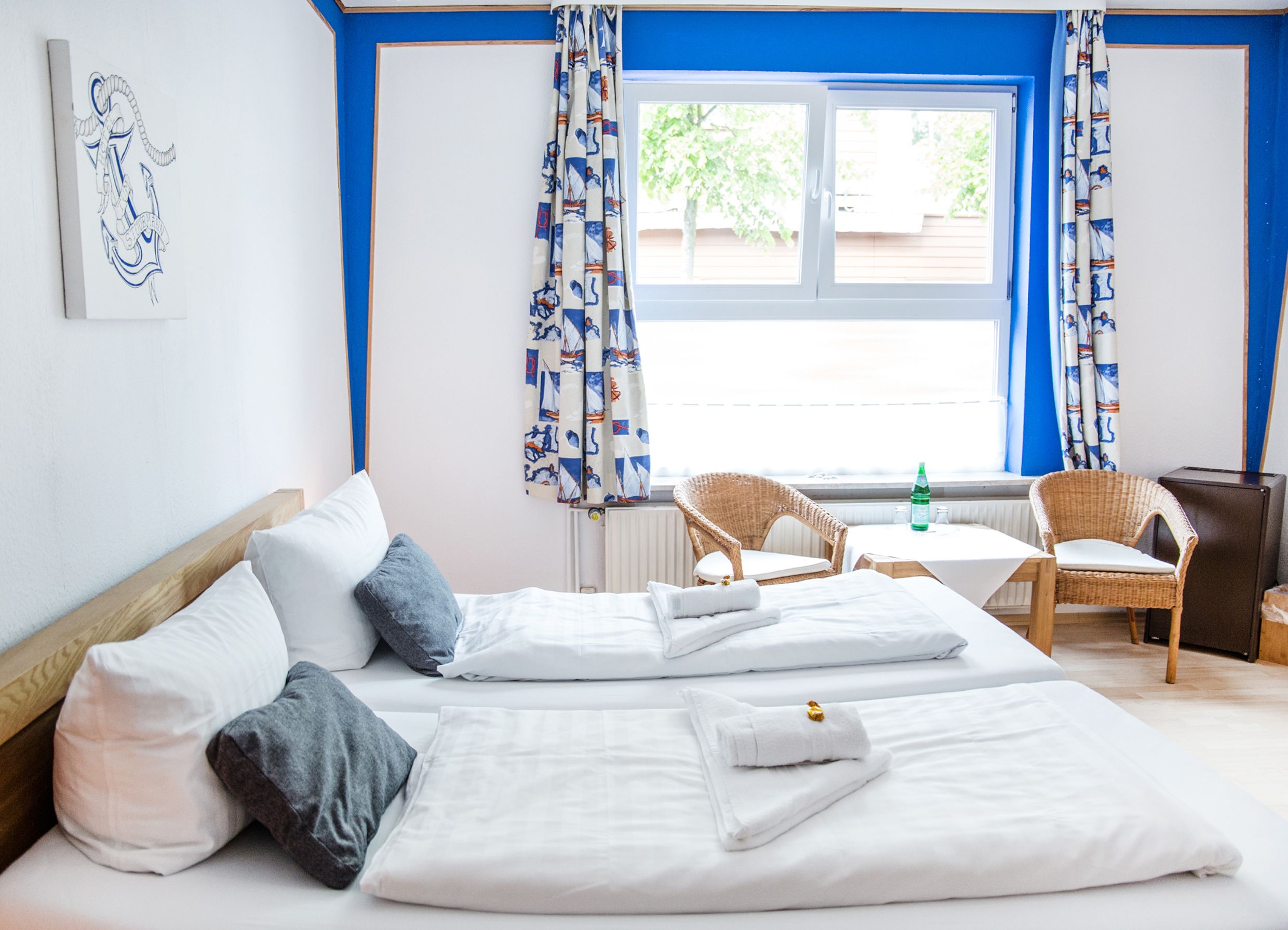 Una habitación de hotel con una cama, dos sillas, una mesa y un ventanal con cortinas.
