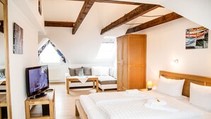 A modern hotel room with a loft-style ceiling, a large bed, a sofa, a wooden wardrobe, and a television on a wooden stand. - Hotel Tum Stüürmann (Büsum)