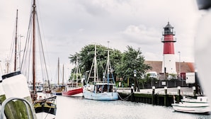 A harbor with boats docked, a lighthouse, and a building with a red roof. - Hotel Tum Stüürmann (Büsum)