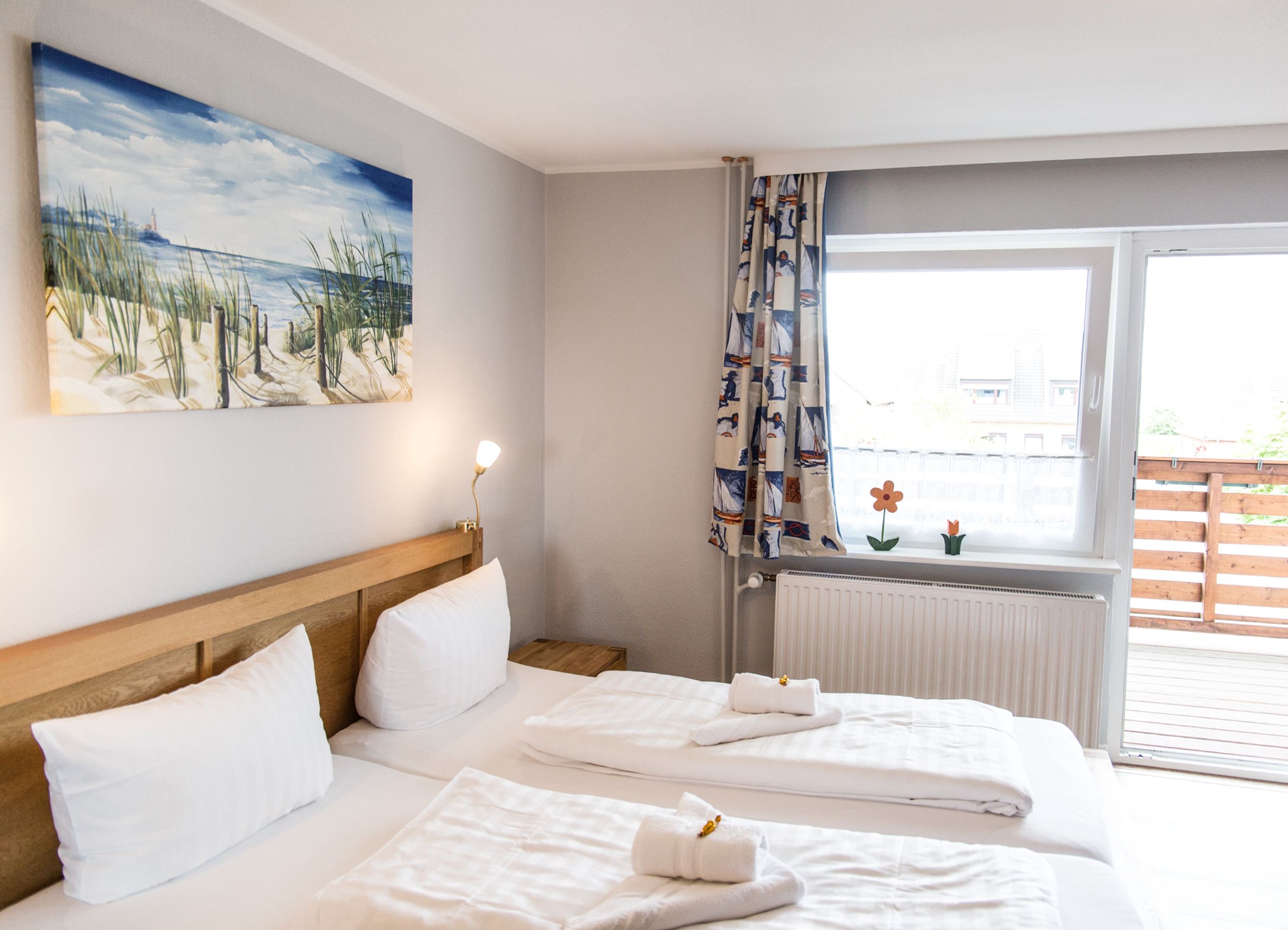 A hotel room with two beds, a painting of a beach, a window with curtains, and a radiator.