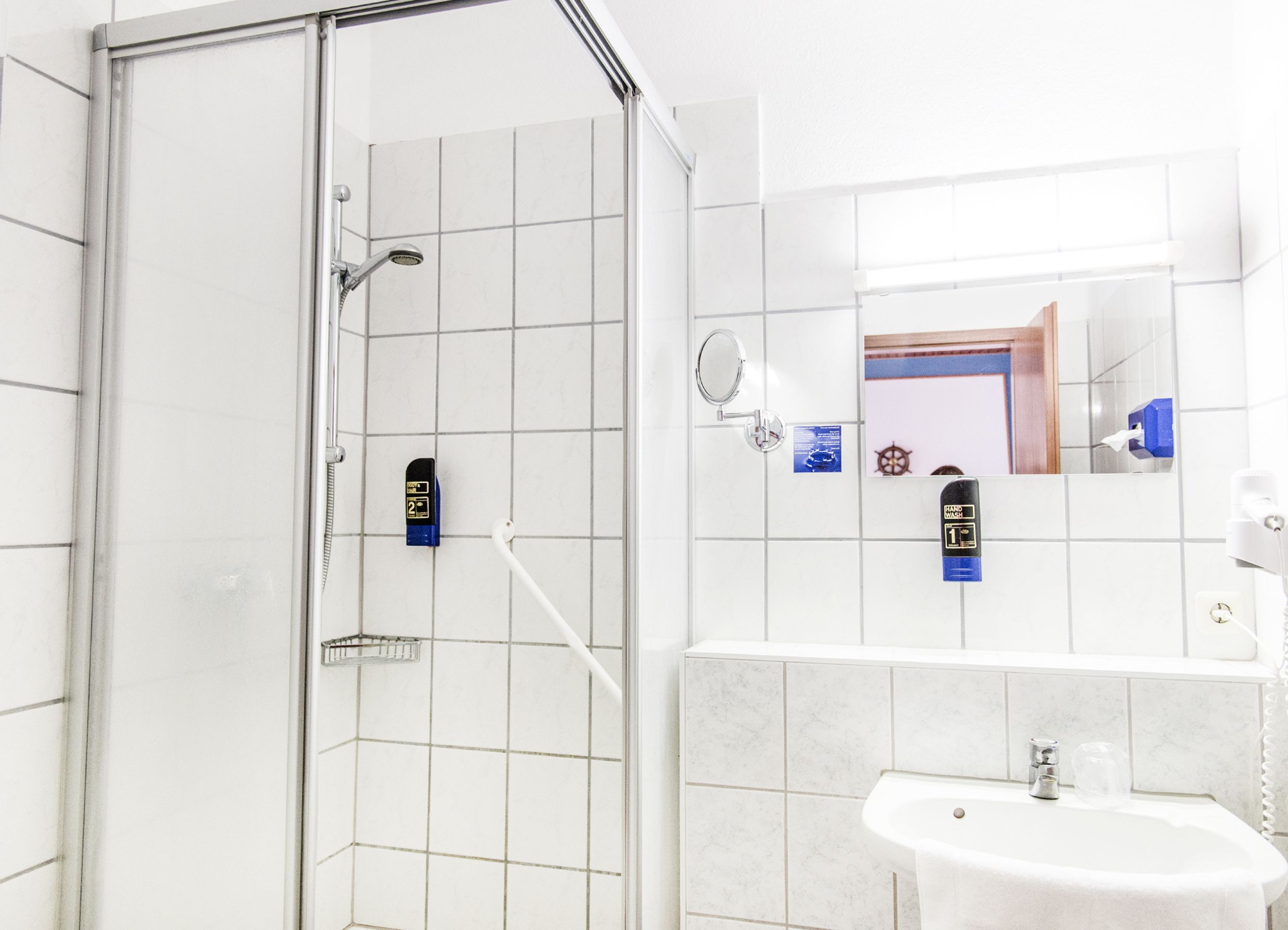 A modern bathroom with a glass shower enclosure, a sink with a mirror, and two hand wash stations.