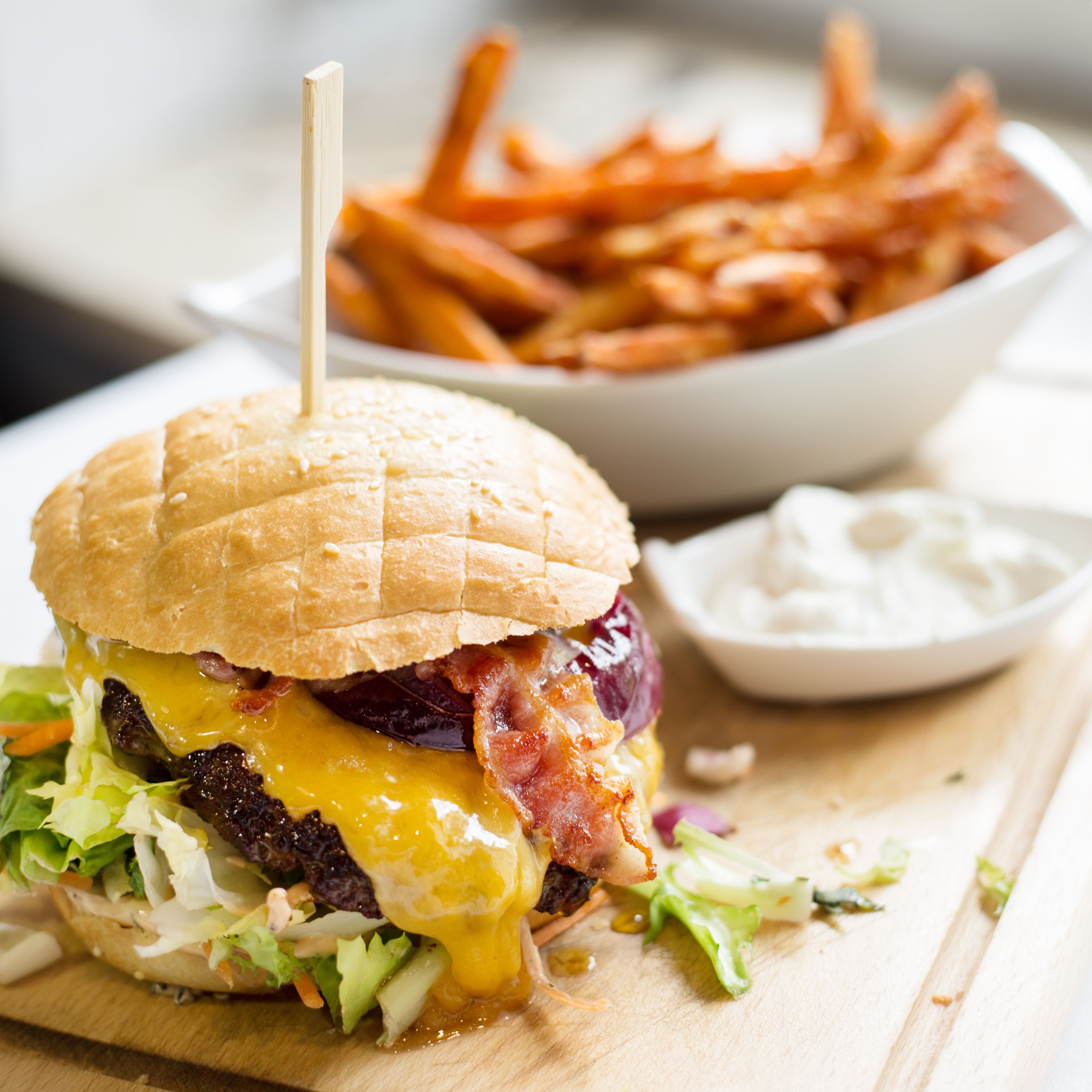 Una hamburguesa con pan, lechuga, queso y tocino, acompañada de papas fritas y un recipiente pequeño de salsa.