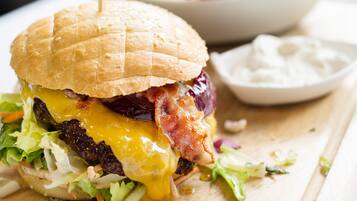 A burger with a bun, lettuce, cheese, and bacon, accompanied by a side of fries and a small bowl of sauce.