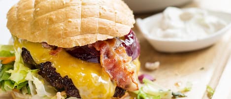Una hamburguesa con pan, lechuga, queso y tocino, acompañada de papas fritas y un recipiente pequeño de salsa.