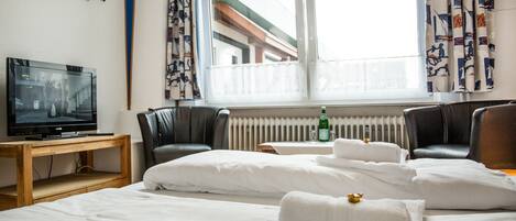 A hotel room with a bed, a desk with a television, a chair, and a window with curtains.