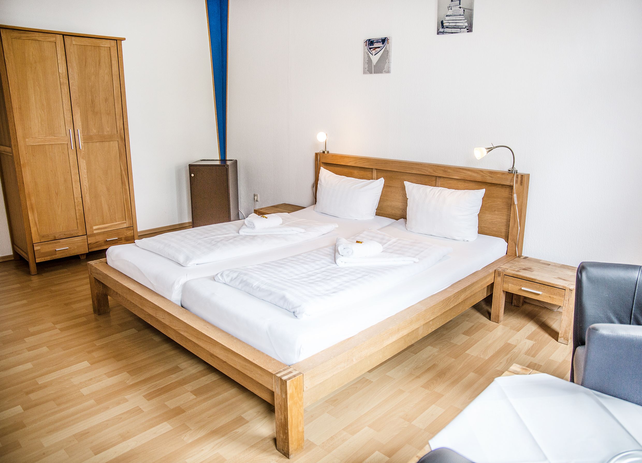 Una habitación de hotel con cama de madera, un armario de madera, una mesita de noche pequeña, una silla y un escritorio.