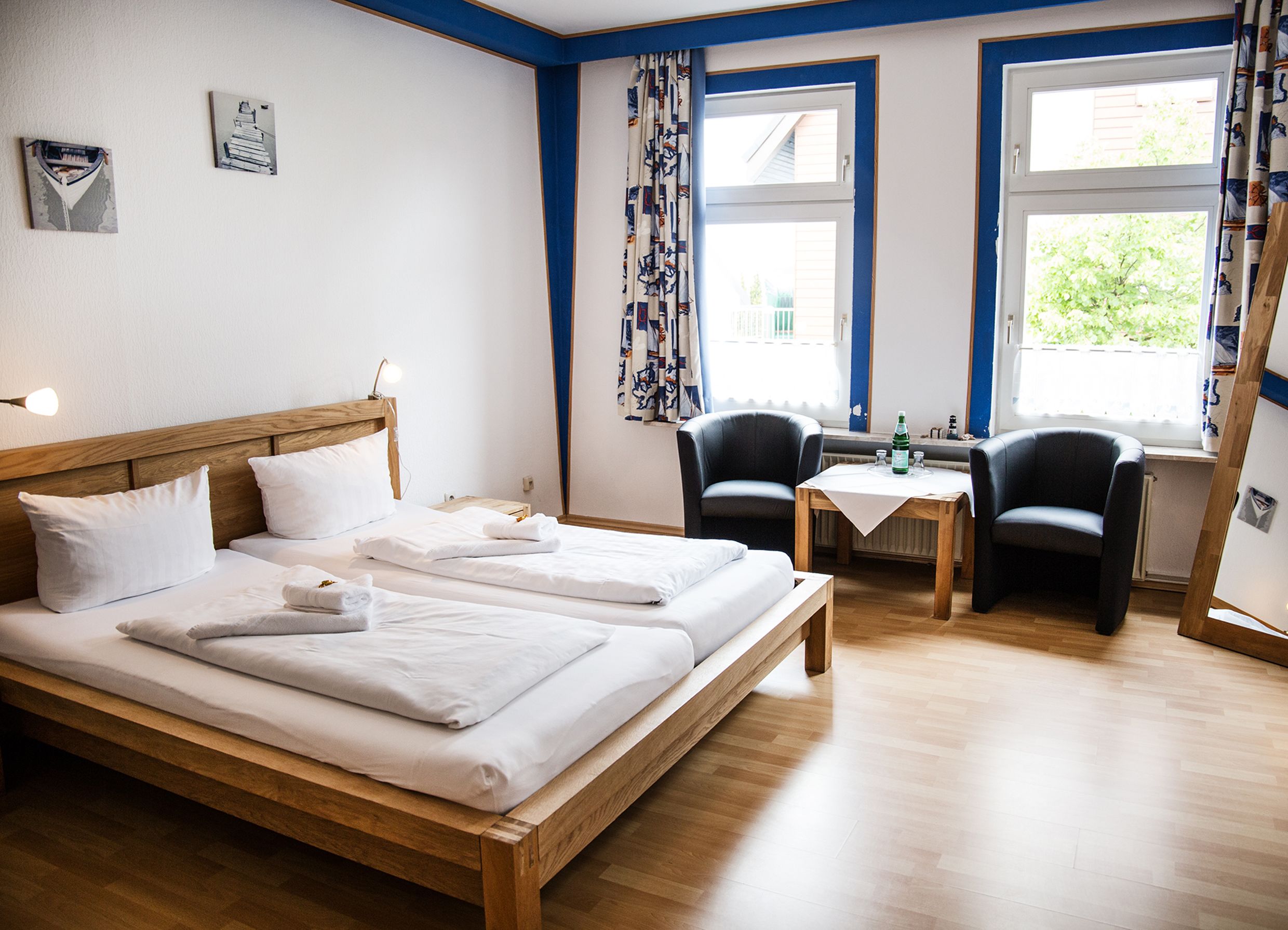 Une chambre d’hôtel avec un lit en bois, deux chaises, une petite table et une fenêtre avec des rideaux.