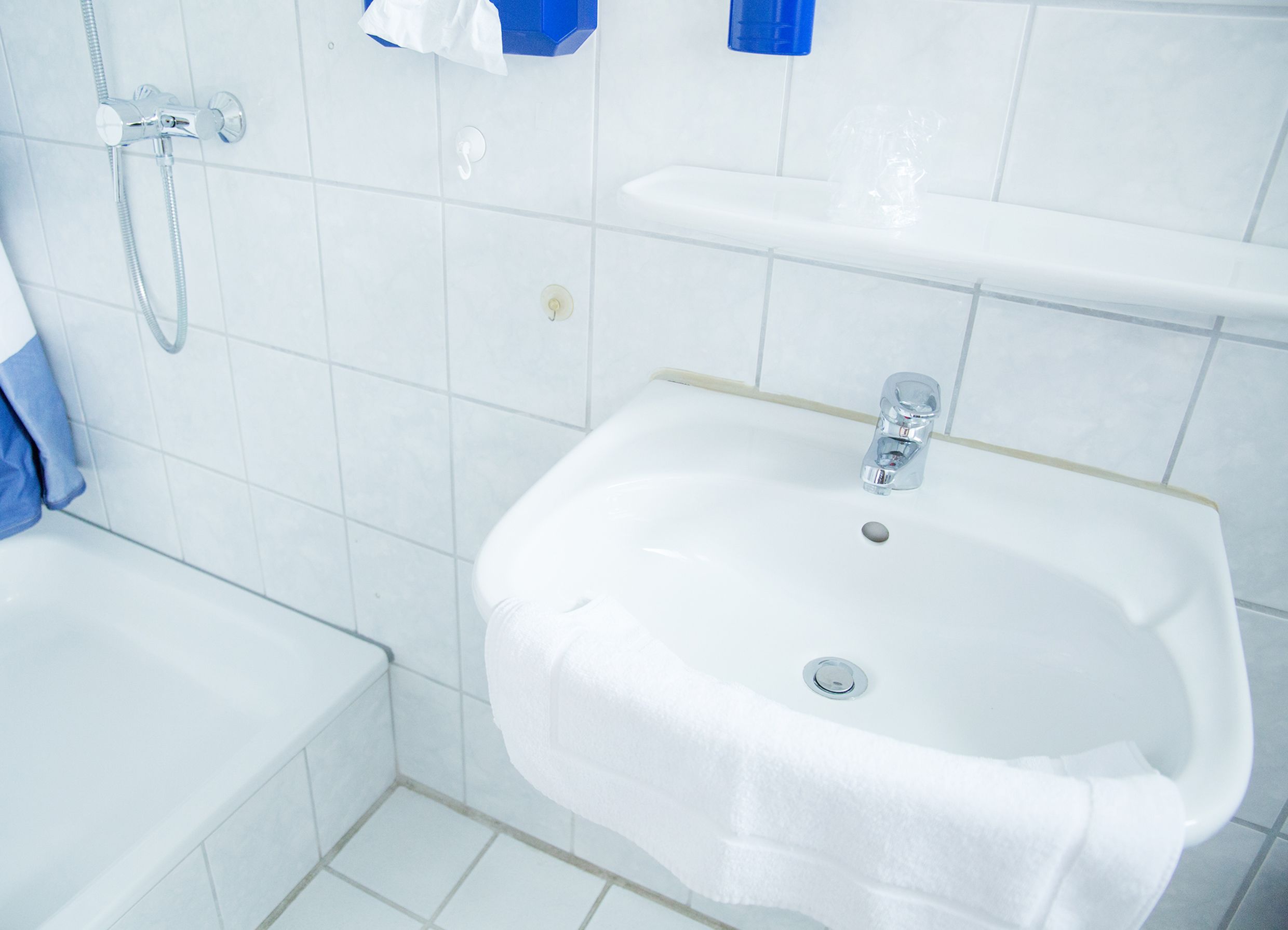 A bathroom with a white sink, a shower, and a blue towel hanging on the wall.
