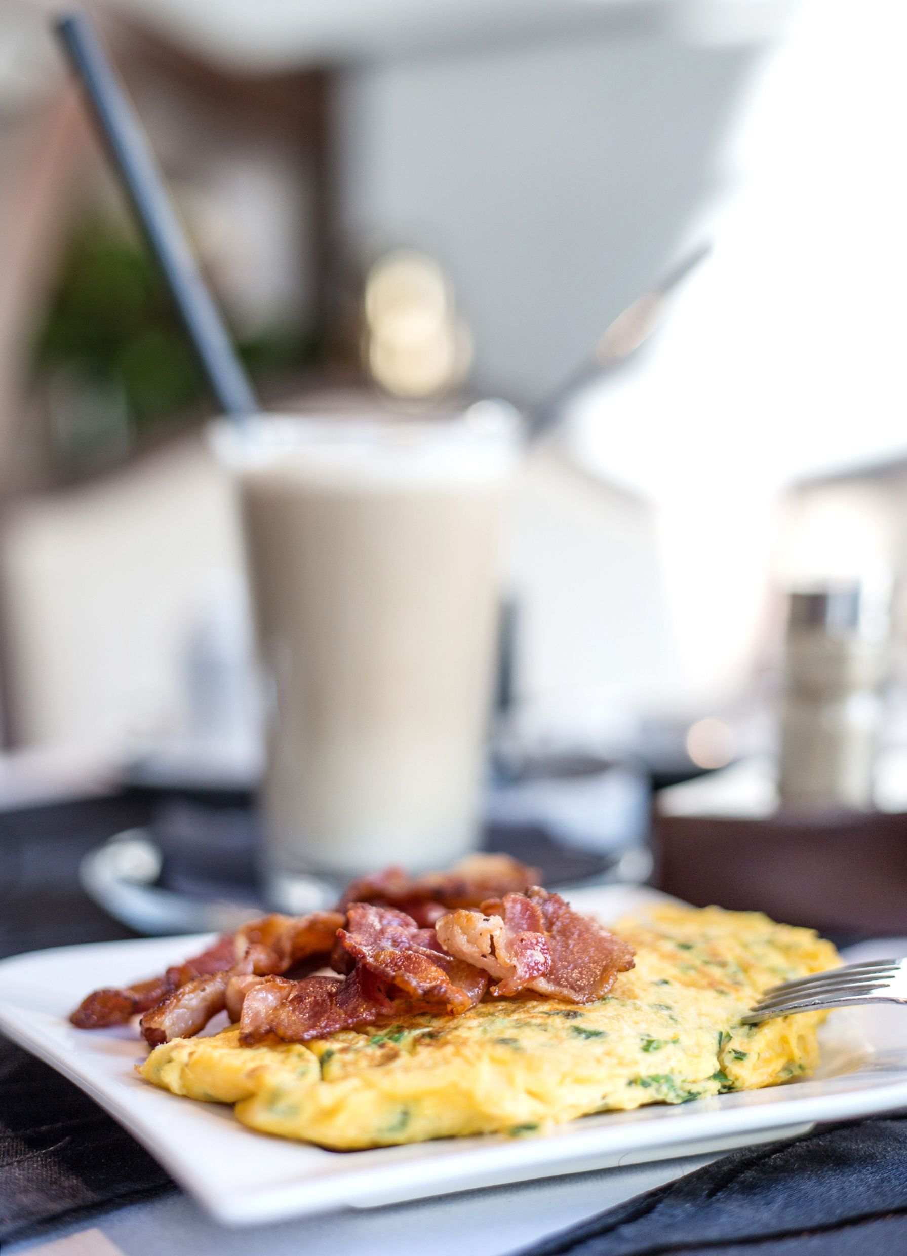 A breakfast plate with eggs and bacon, a glass of milk, and a fork on a table.