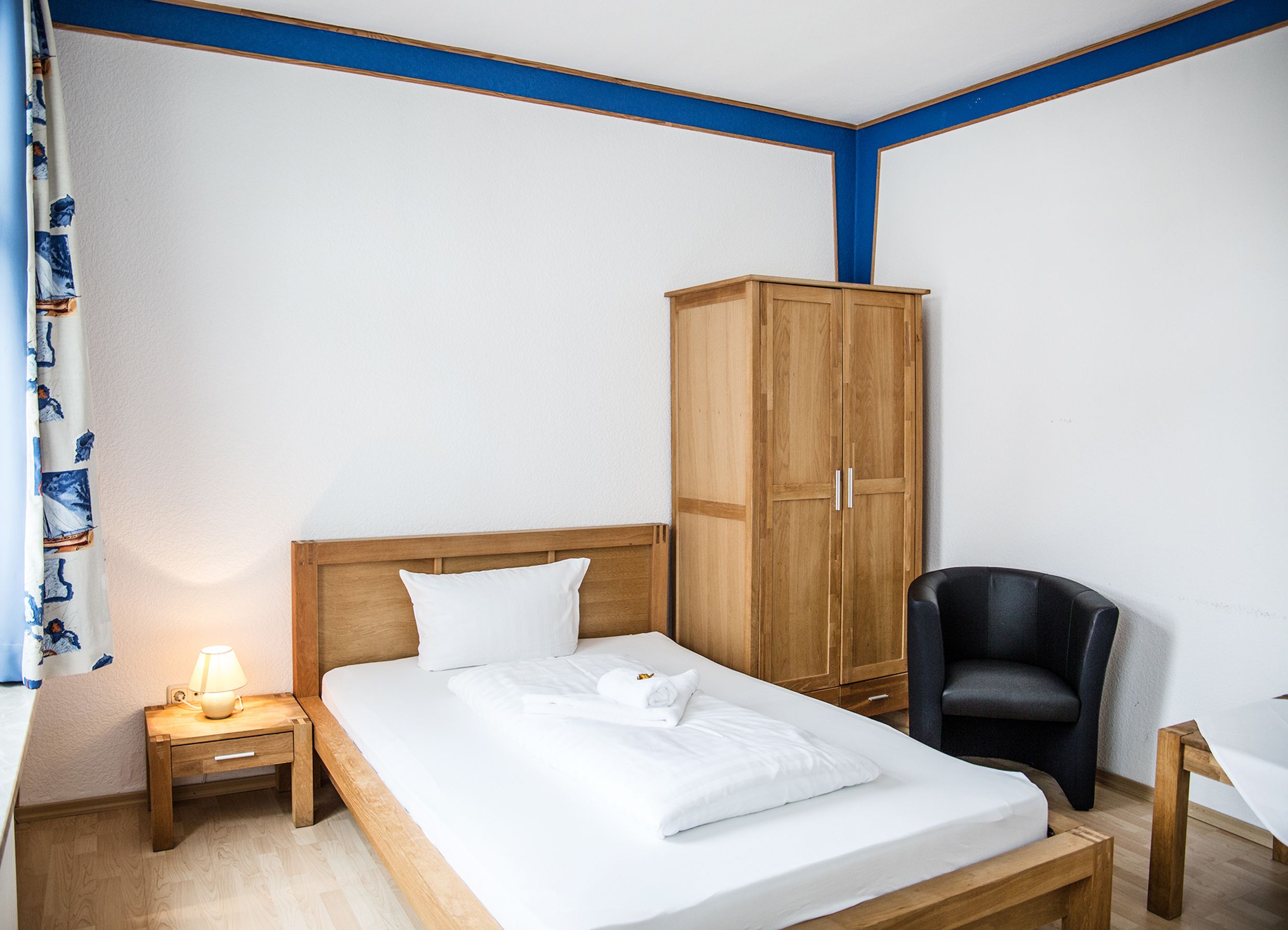 Un dormitorio con una cama de madera, una mesita de noche con una lámpara, un armario, una silla negra y un escritorio.