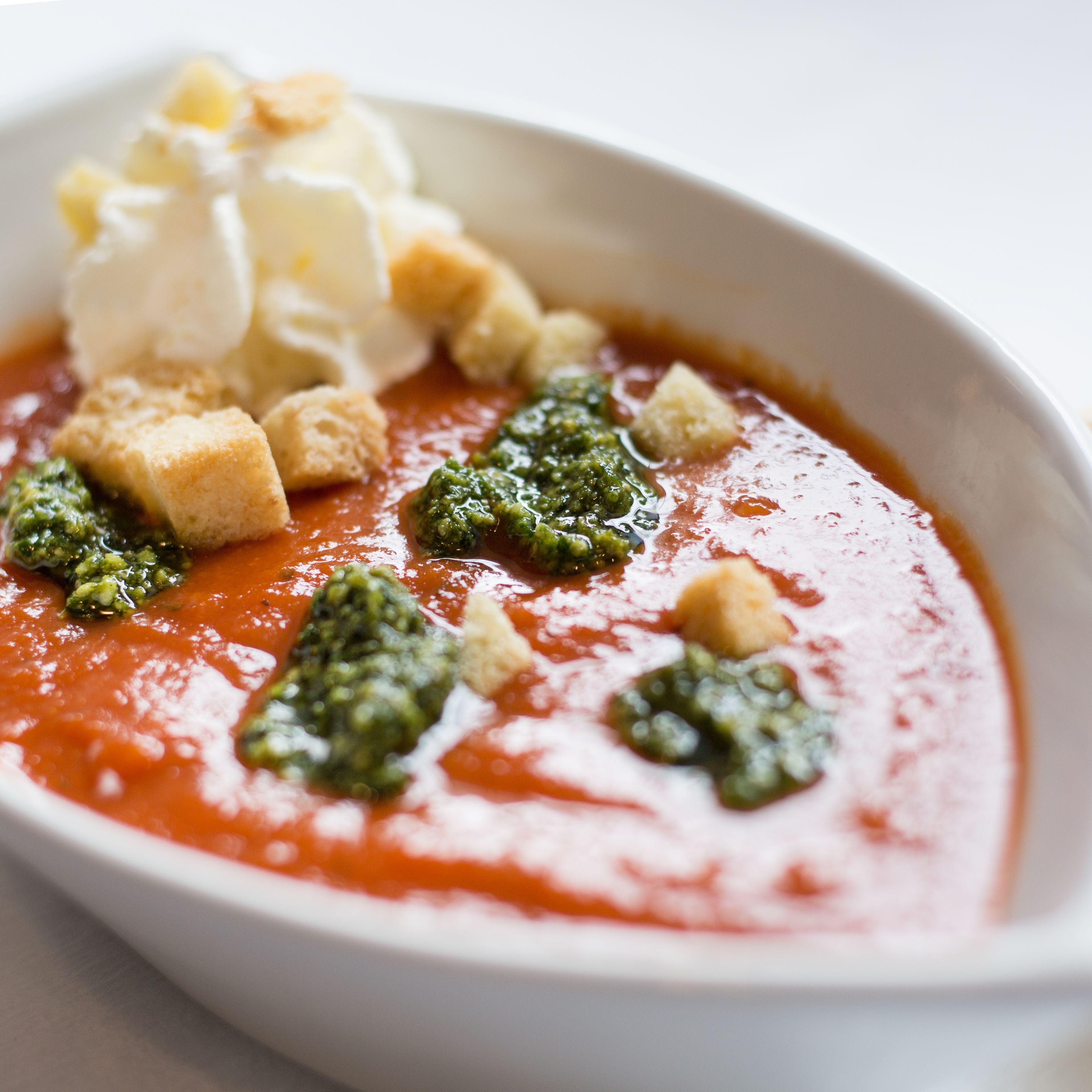 A bowl of tomato soup with croutons and a dollop of cream.