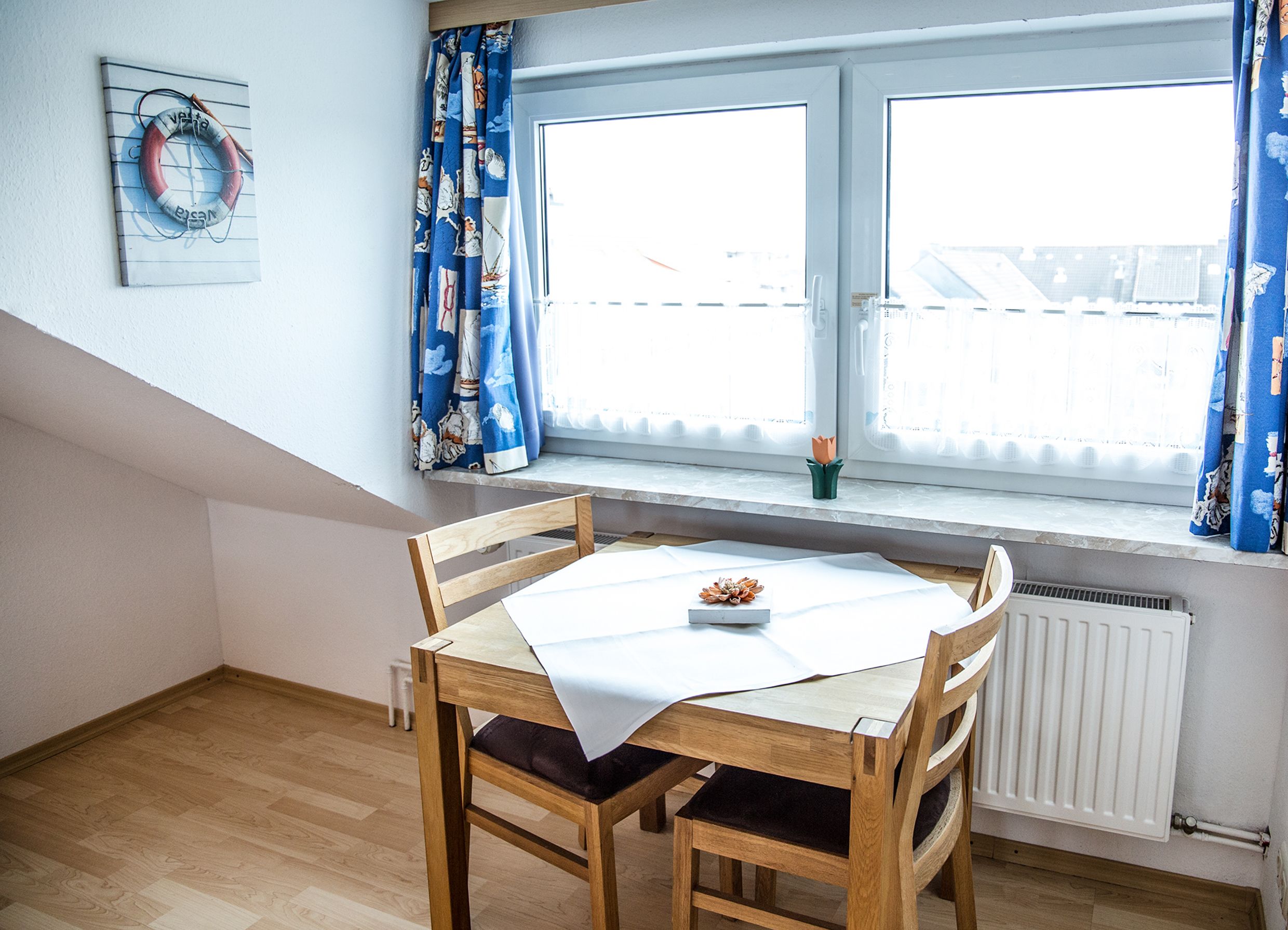 Ein Essbereich mit Holztisch und Stühlen, einem Fenster mit Vorhängen und einem Heizkörper darunter.