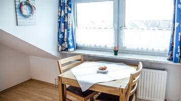 Ein Essbereich mit Holztisch und Stühlen, einem Fenster mit Vorhängen und einem Heizkörper darunter.