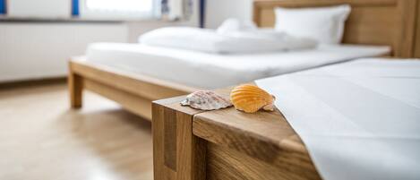 A neatly made bed with white linens and pillows, a wooden headboard, and two seashells on the side.
